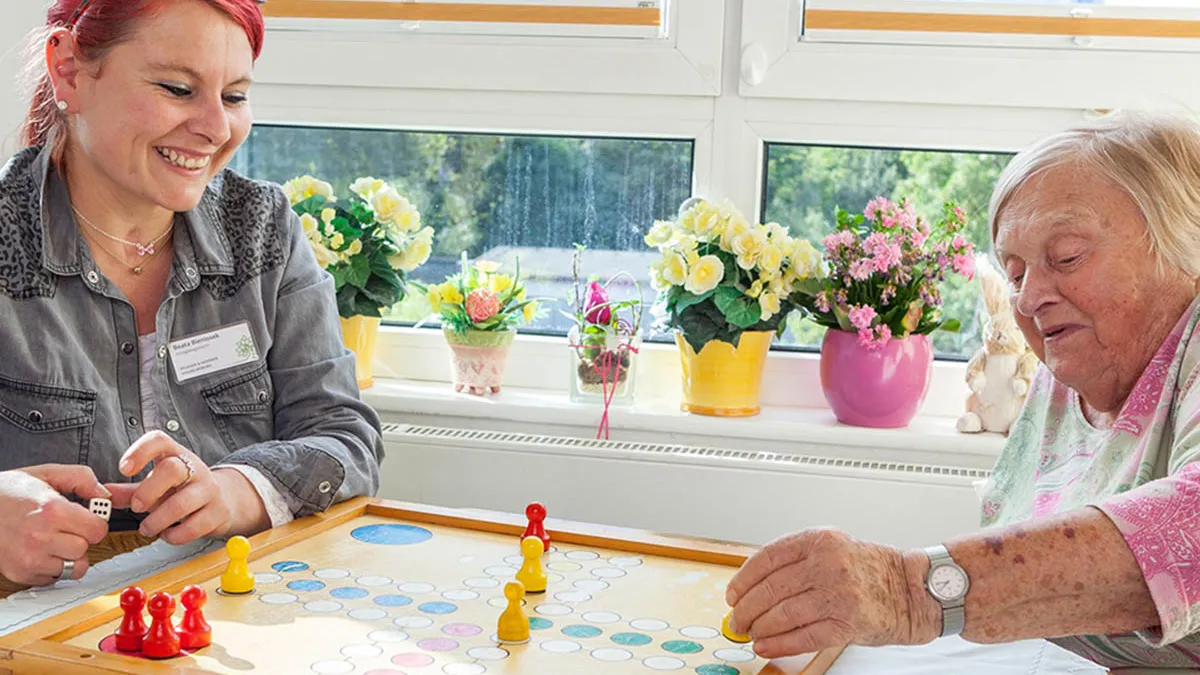 Eine Seniorin in der PFLEGEN & WOHNEN HAMBURG Einrichtung in Wilhelmsburg beim Gesellschaftsspiel spielen mit einer Betreuerin.