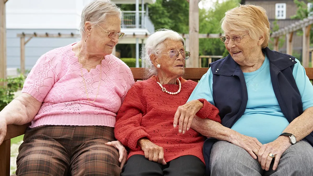 Drei Bewohnerinnen sitzen in vertrautem Miteinander gemeinsam auf einer Bank auf der Terrasse.