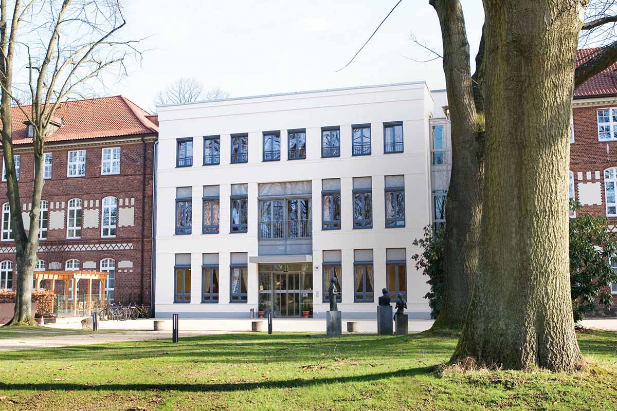 Das Hauptgebäude von PFLEGEN & WOHNEN HAMBURG in Farmsen liegt inmitten alter Bäume mit Fokus auf Demenz und Schwerstpflege.